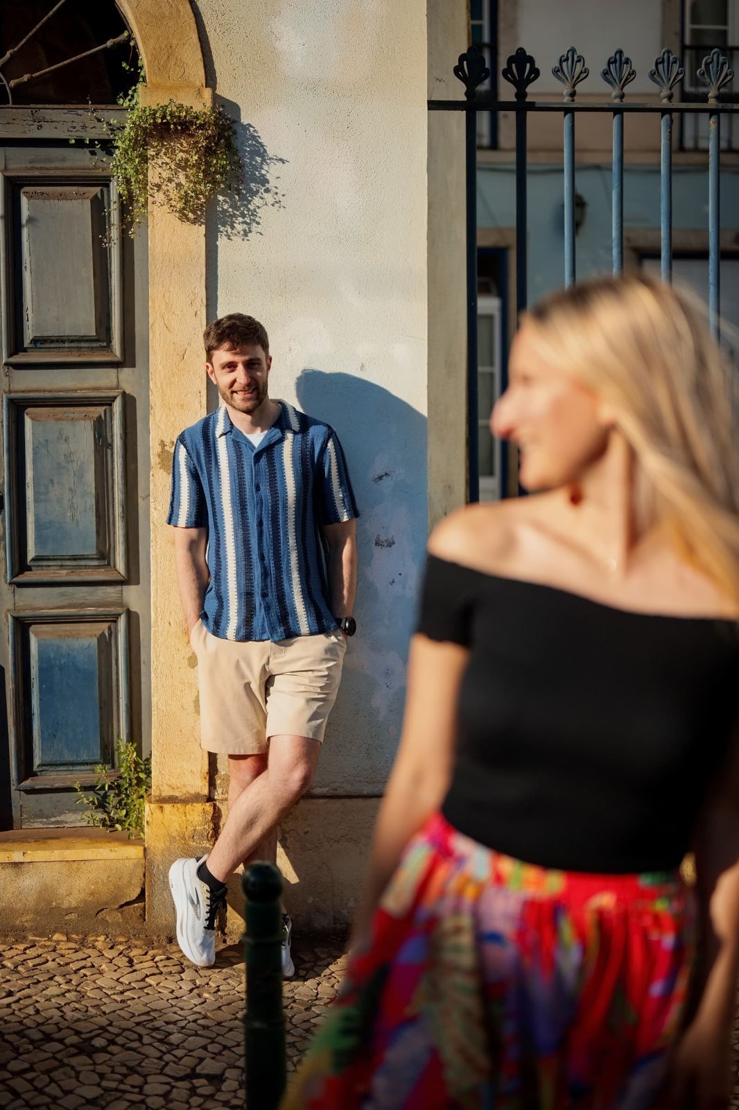 Man leaning in a doorway in warm evening light while his partner walks past in the foreground