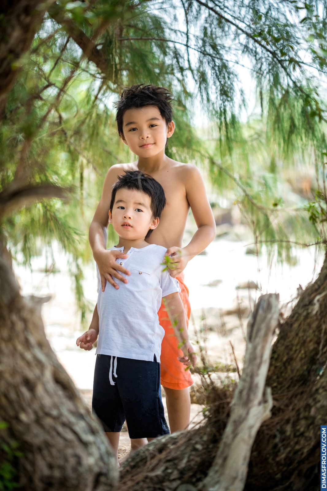 Older brother hugging his younger sibling under trees near the beach