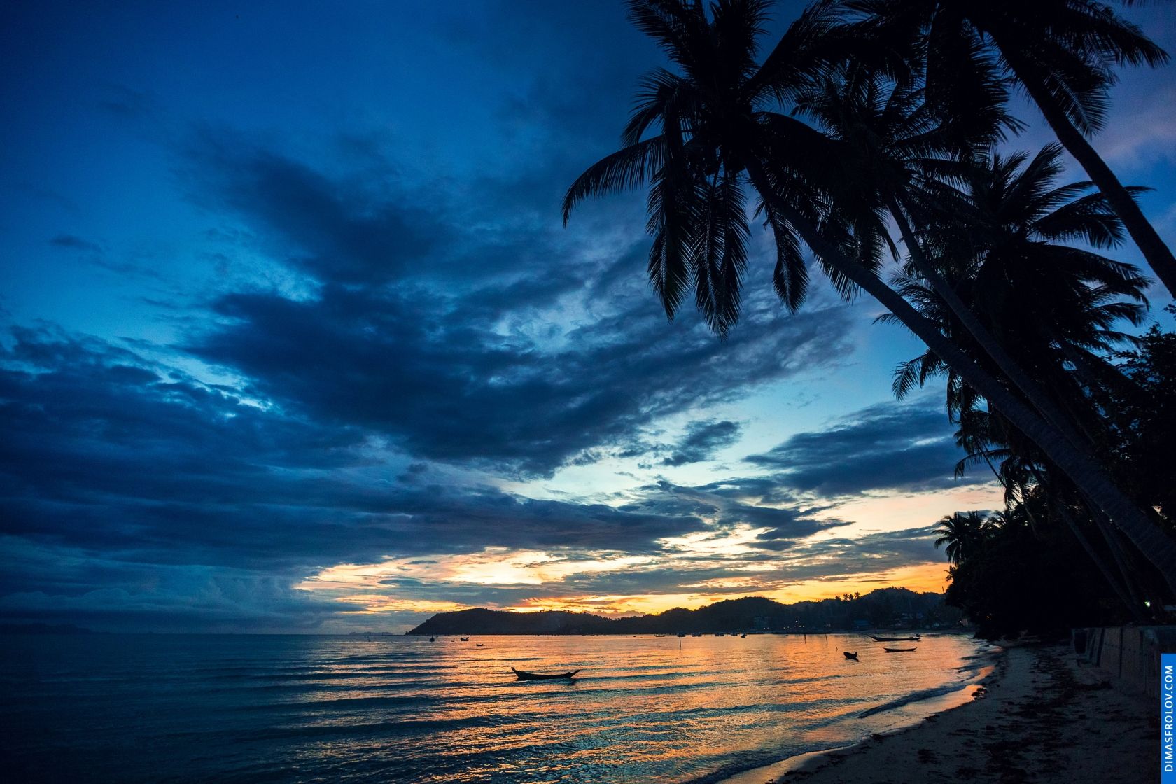 Moody twilight scene on a tropical beach with dark clouds and a strip of golden light on the horizon