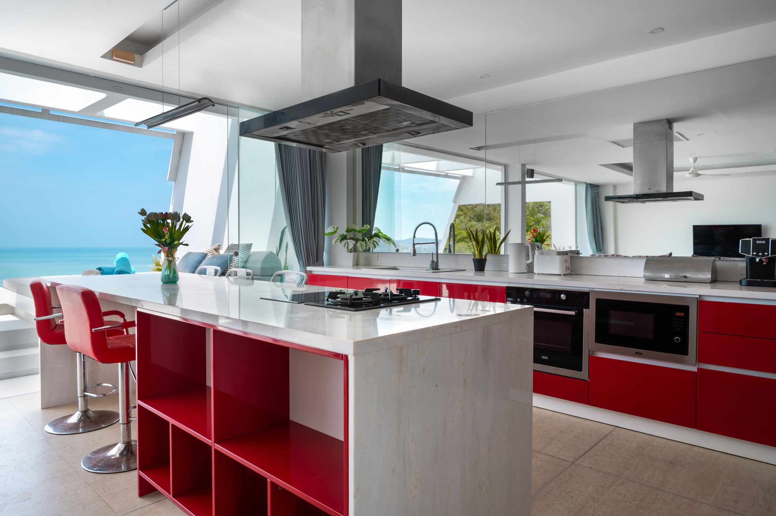 An open-plan kitchen with a red island and a sea view through floor-to-ceiling windows